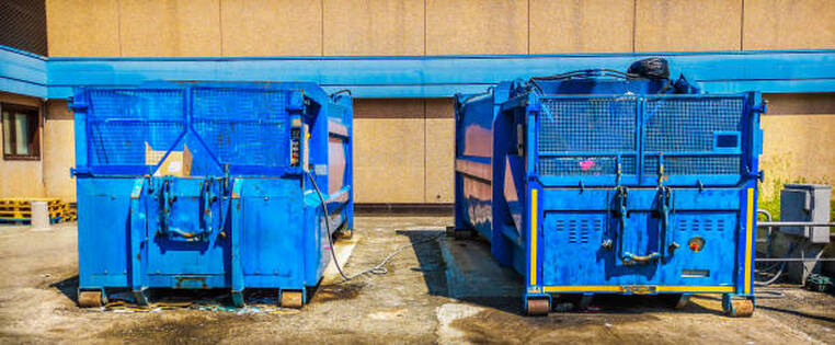 Two large blue dumpster rentals in a business parking lot.