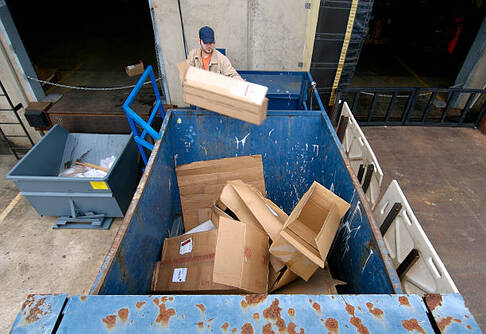 A person loading cardboard into a dumpster in Norwalk, CT.